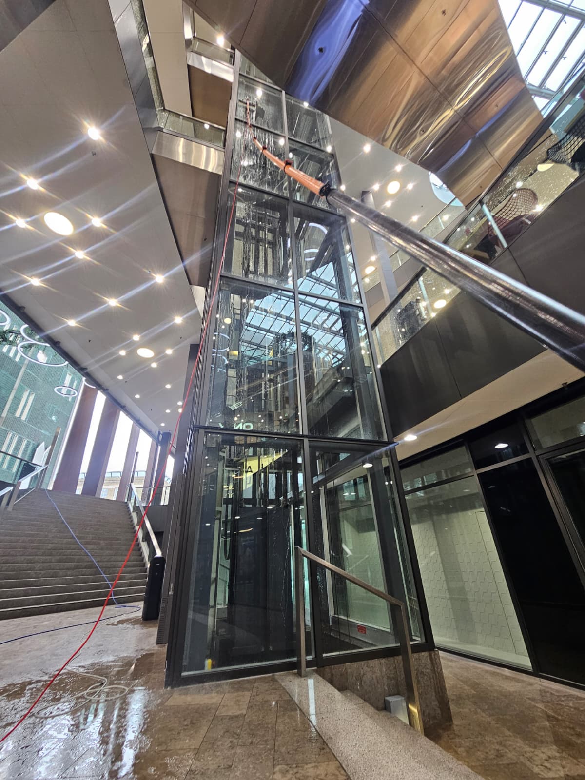 Glazen liftschacht in een atrium gereinigd met telescoopsteel